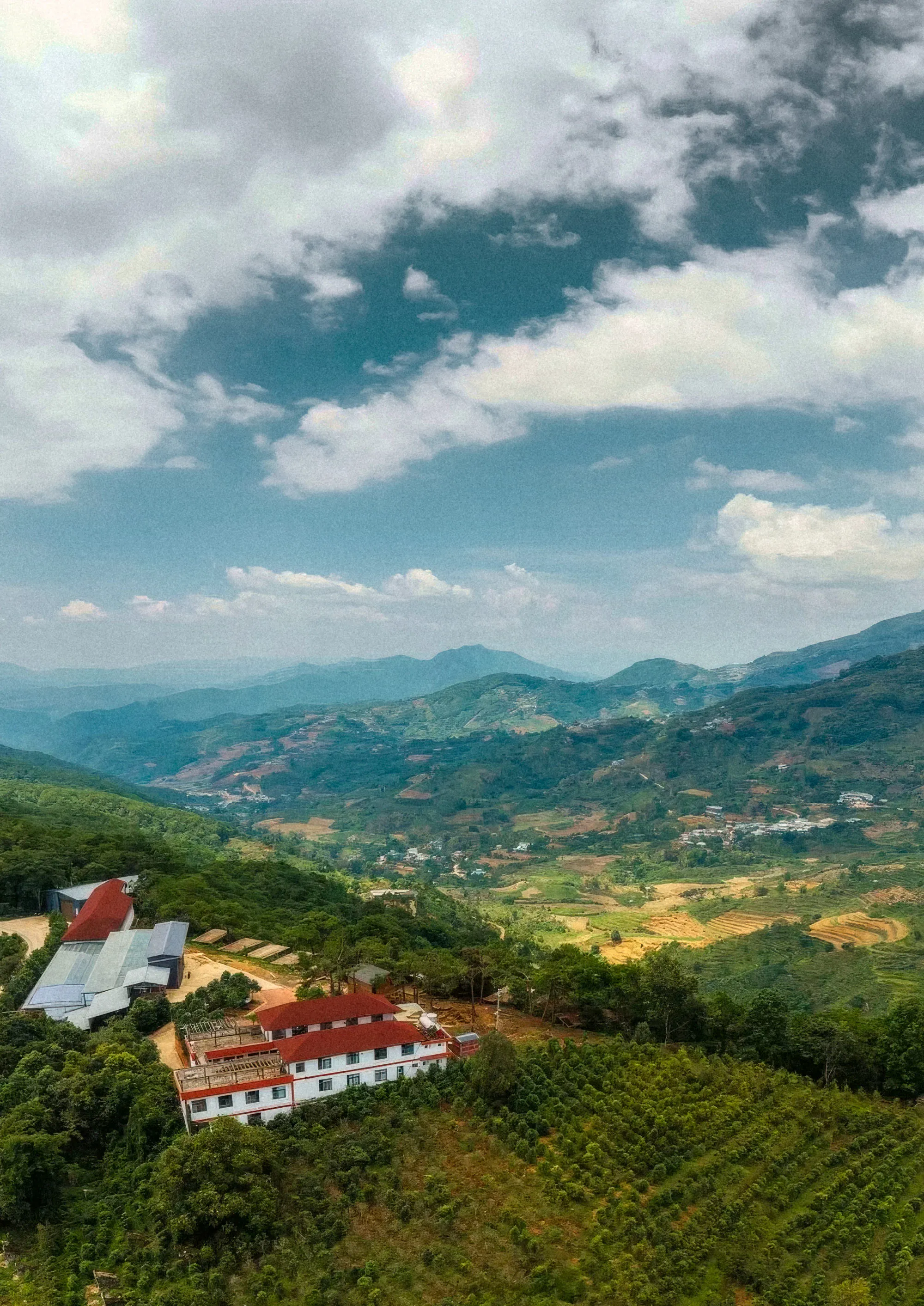 Vue aérienne d’une vallée du Yunnan : la ferme et ses hangars au premier plan, les parcelles de caféiers et les montagnes au fond